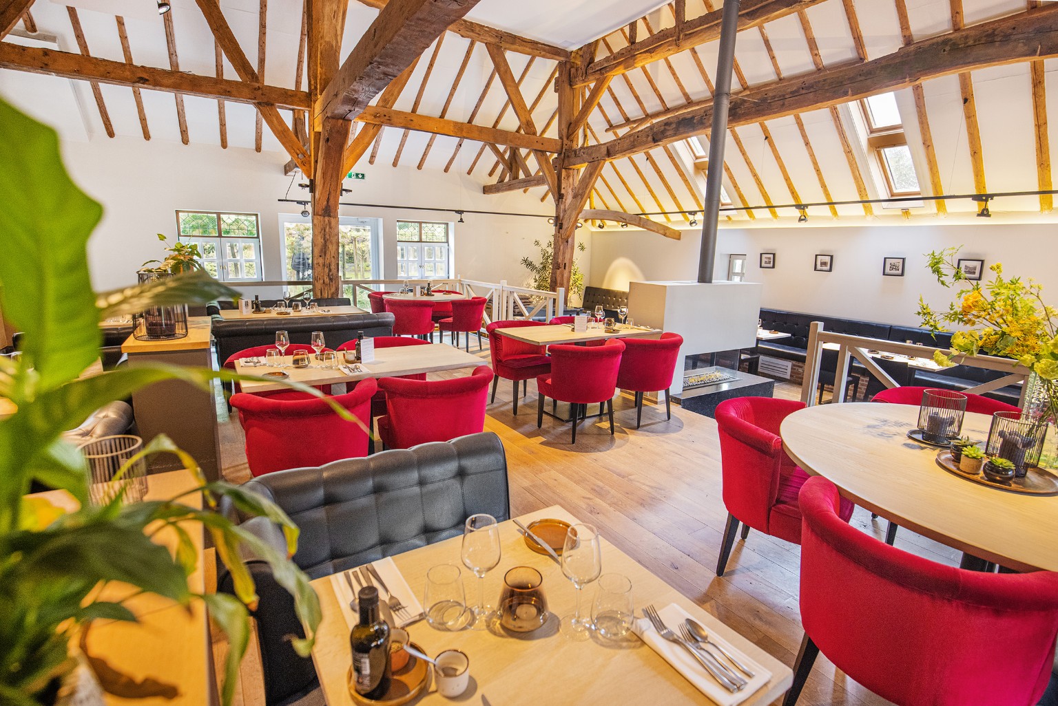 Het interieur van Mangerie Weselo met houten balken, rode stoelen en gedekte tafels
